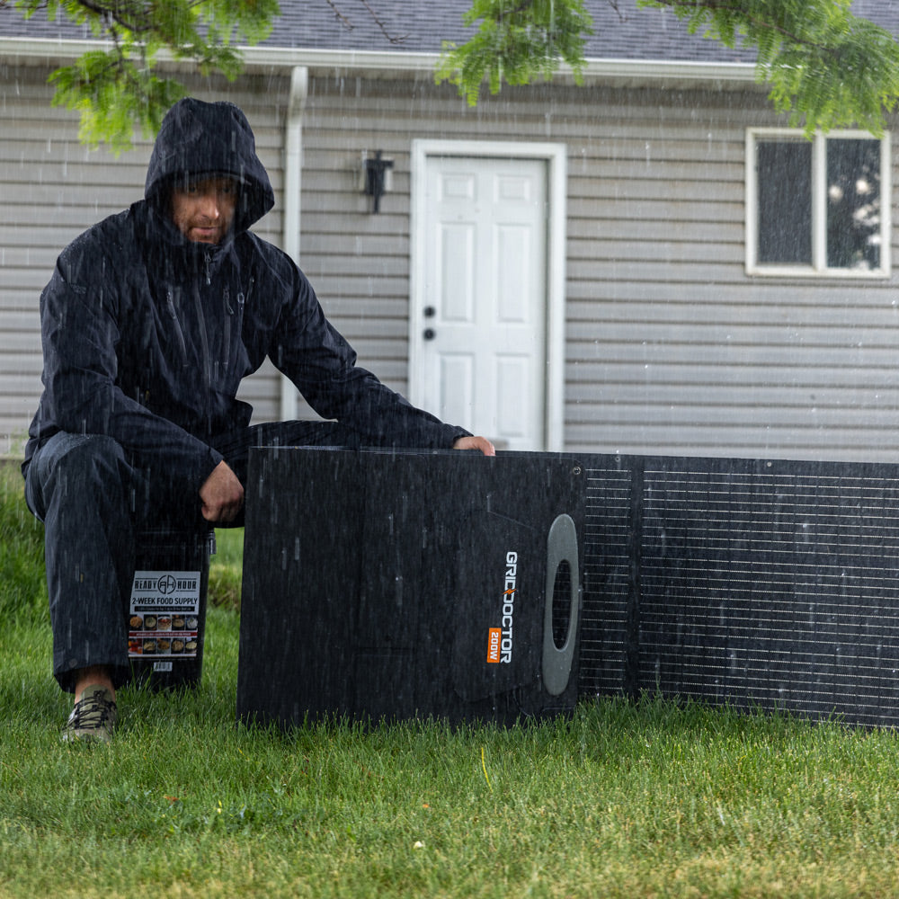 A man sits in the rain on a bucket of preparedness food. He sets up the included 200W Solar Panel.