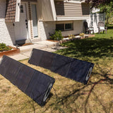 Two solar panels on a grassy area in front of a house